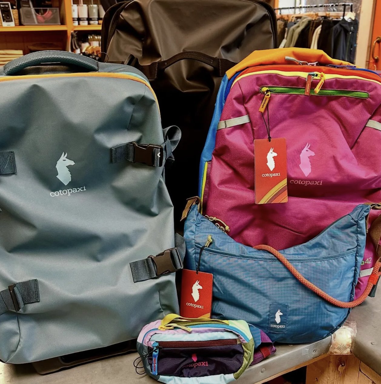 Colorful Cotopaxi backpacks, a sling bag and a hip pack on display