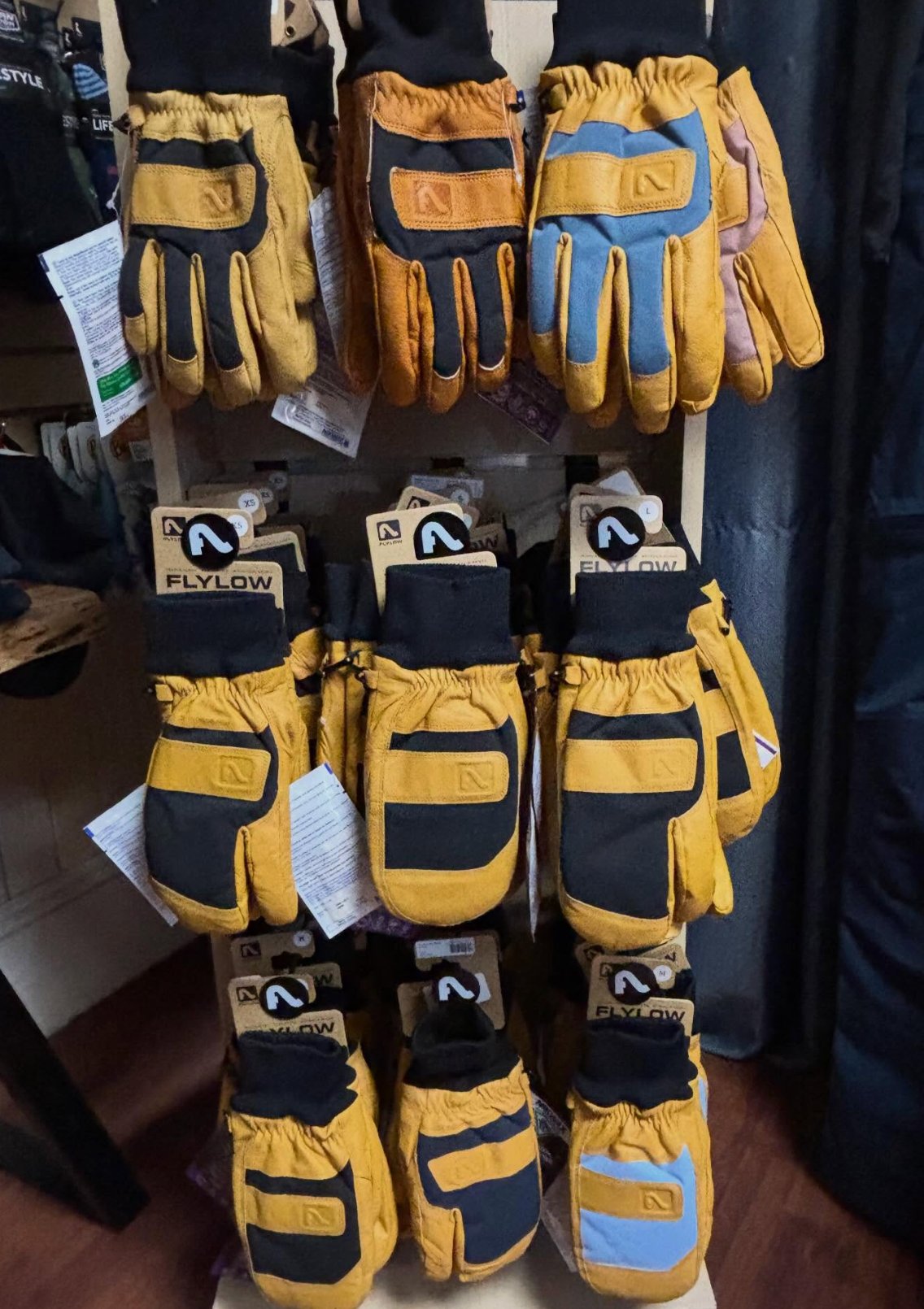 Tan and black Flylow leather ski gloves and mittens on a rack