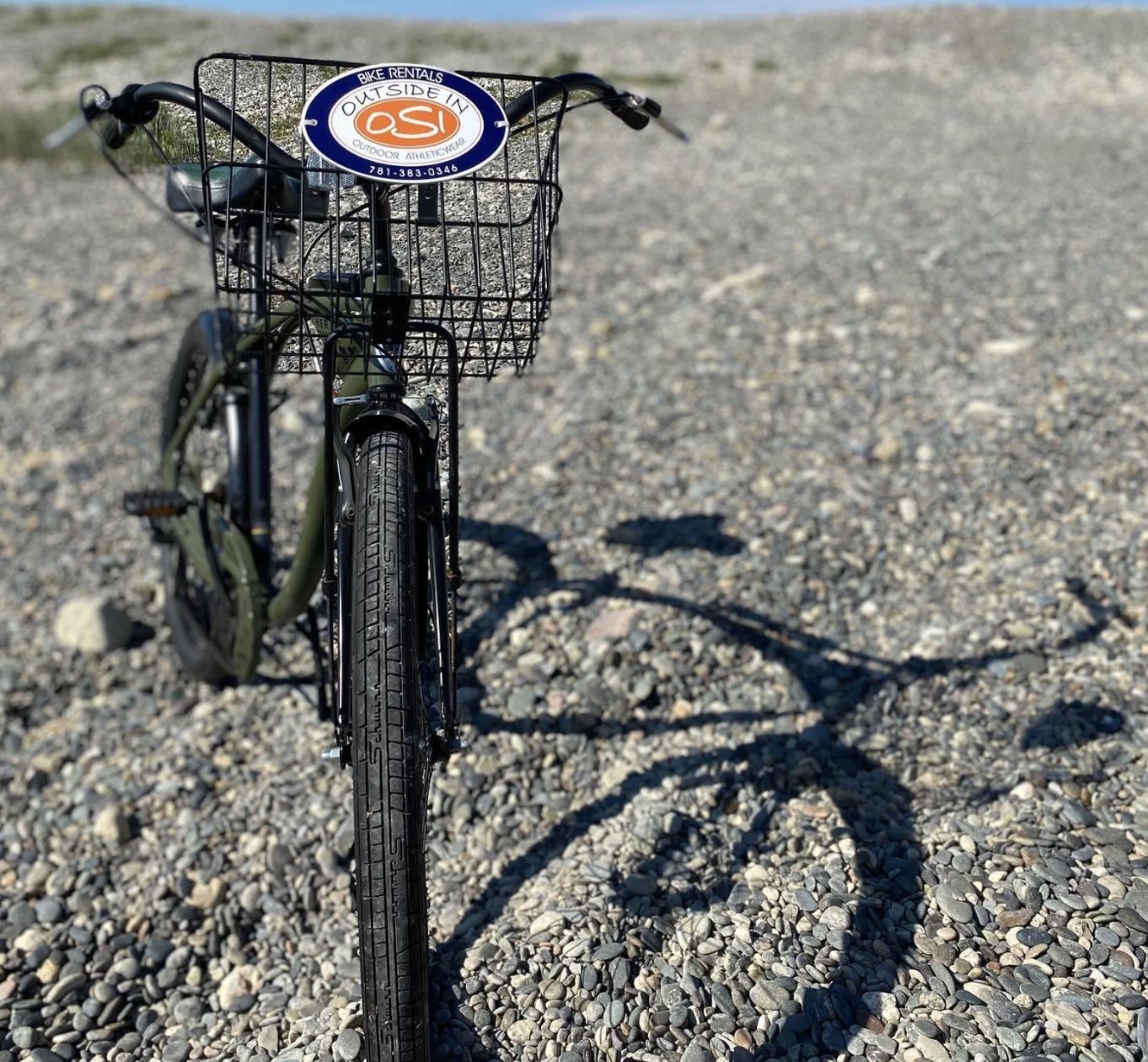 An Outside In rental bike with an OSI basket sign parked on the beach