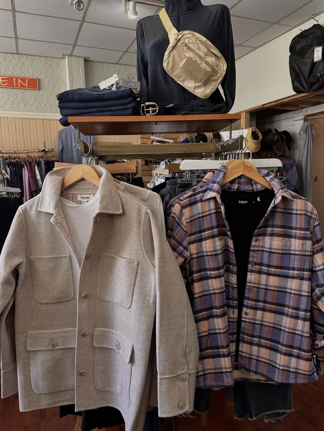 A wool shacket and plaid flannels hanging on wooden hangers